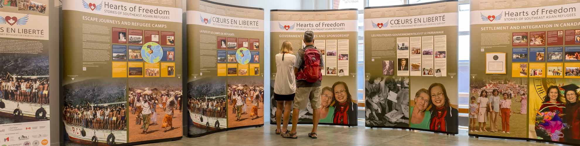 Two people stand in front of five exhibition panels, displayed in both English and French.