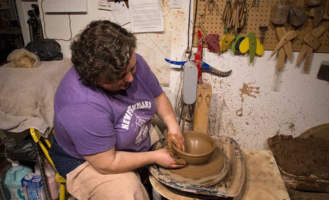 Woman in black tee shirt works on molding another piece of pottery on the wheel.