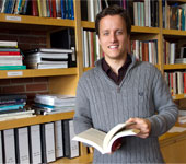 A man stands in front of floor to ceiling bookshelves.
