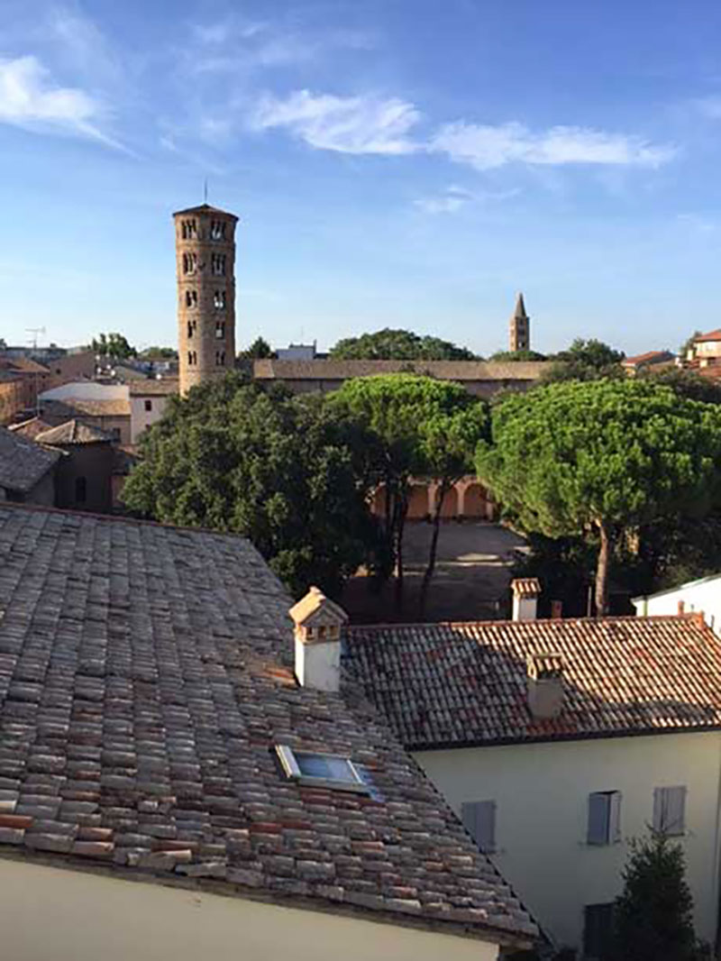 Looking out over roof tops of the city of Revenna, houses have shingles made of clay, and there is an ancient tower on the horizon.