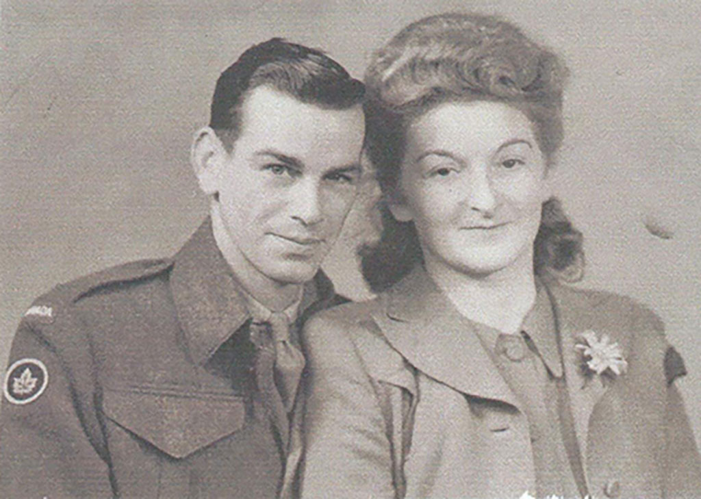 Old portrait with a young man in uniform, leaning in towards a woman in a nice suit with a flower on her lapel.