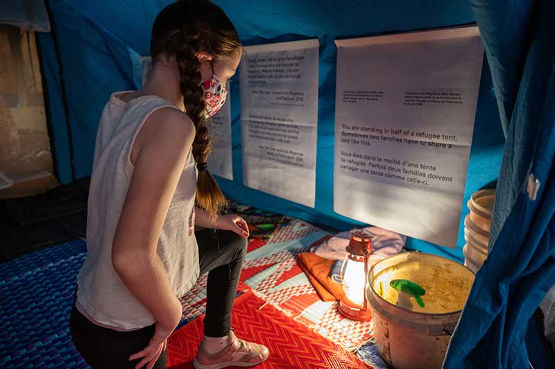 A 10-year-old girl reads panels inside a refugee camp tent.