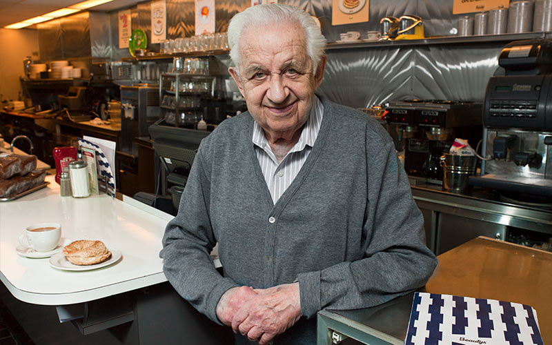 A man in a grey sweater stands in a restaurant.