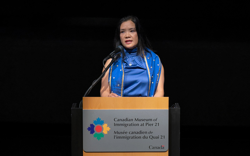 A woman speaks into a microphone at a podium with the Museum’s logo on it.
