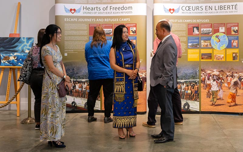 Three people stand and talk in front of the exhibition panels.