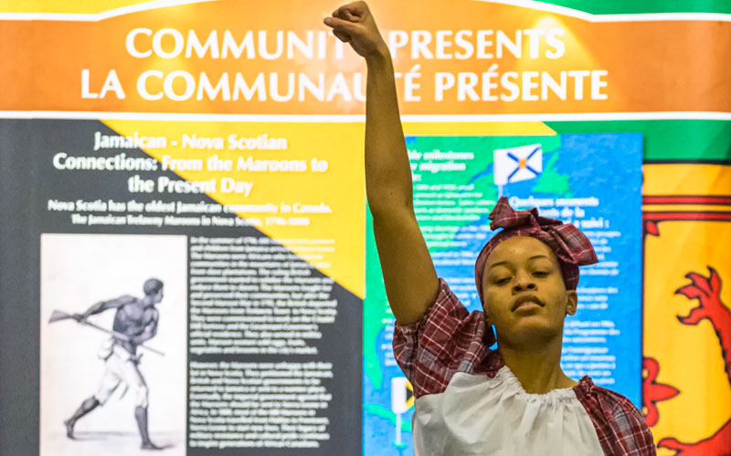 A person in costume raises their fist with the exhibition in the background.