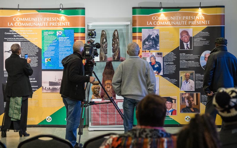 Four people look at the exhibition, including one person with professional camera equipment.