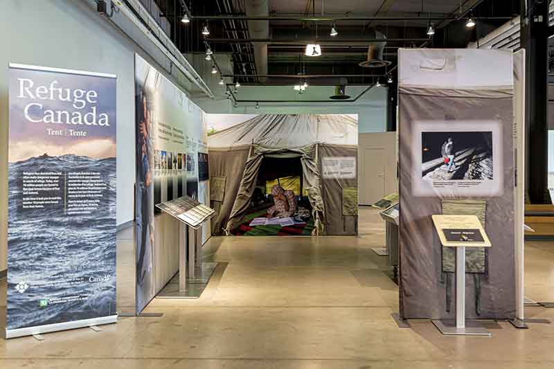 Popup banner with Refuge Canada written out over a background of a dark and stormy sea. Panels and kiosks are configured to fit in a small floor plan.