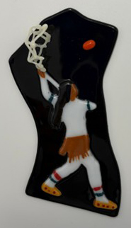 Fused glass piece depicting a Haudenosaunee man, in traditional clothing holding a crosse (lacrosse stick) high above his head ready to swing at a red lacrosse ball in the air.