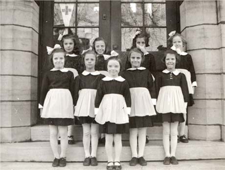 Nine young girls in uniform on the steps of a stone building.