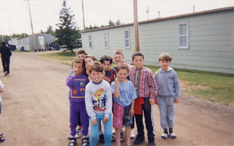 A group of Kosovar refugee children pose on a dirt path, several of them holding up peace signs.