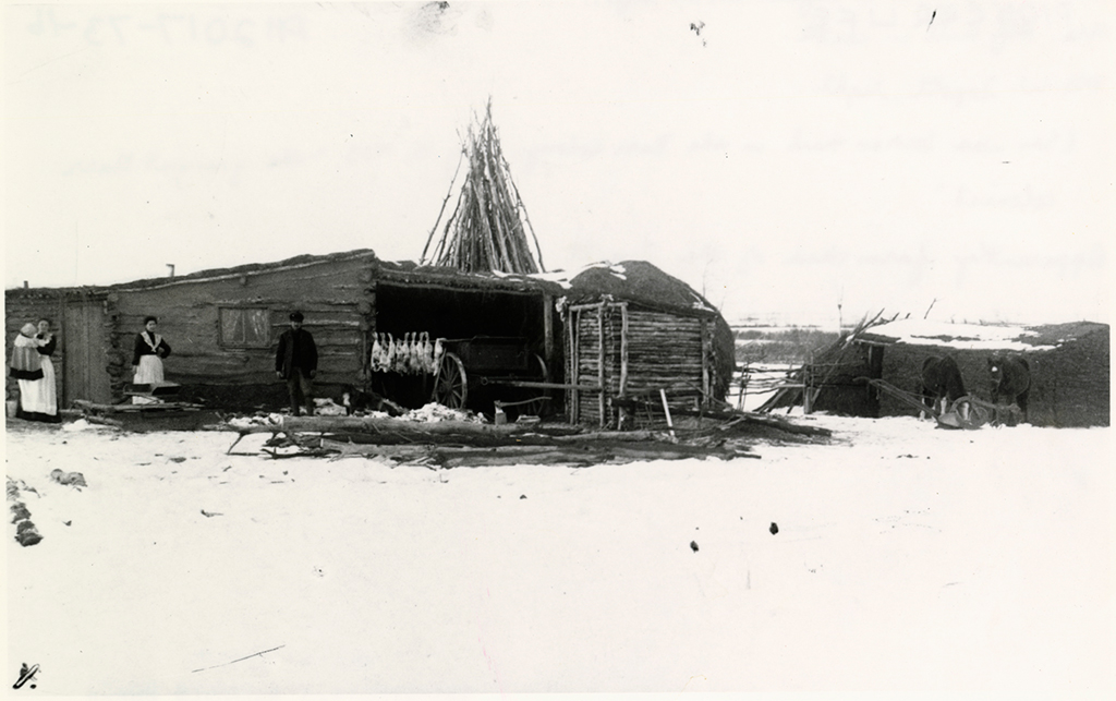 An old homestead with people dressed in clothing for winter.