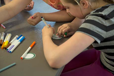 A young girl draws with a marker on a small circle of paper.