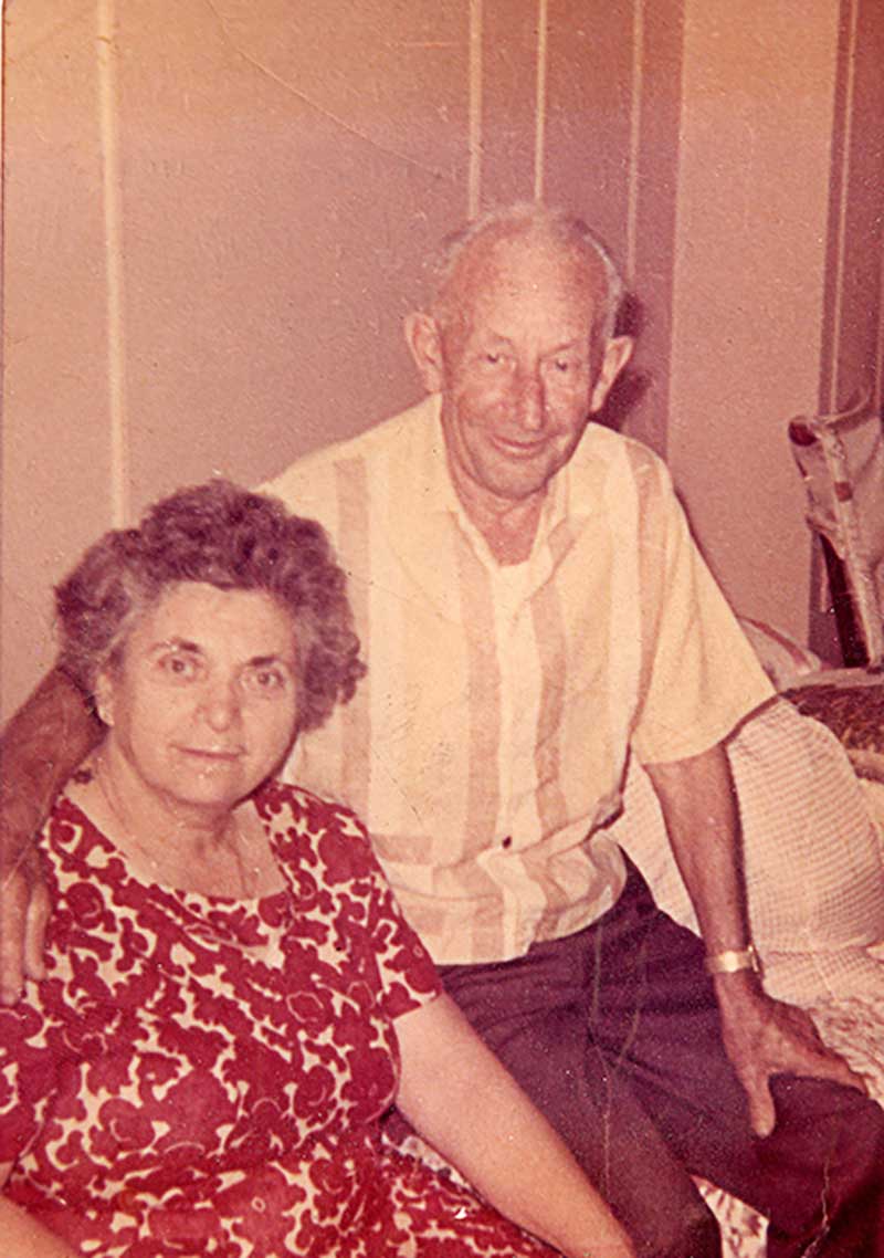 A woman sits on a couch, her husband sits next to her with his arm around her shoulder.