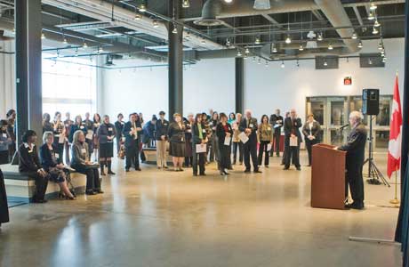 Some people are standing and some are sitting while they all listen to a speaker.