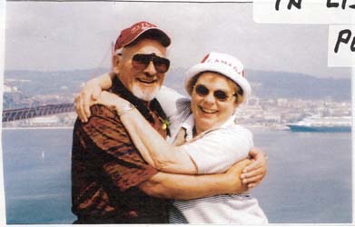 Recent coloured photo of Ursula and Manfred hugging, water and cruise ship seen in background.