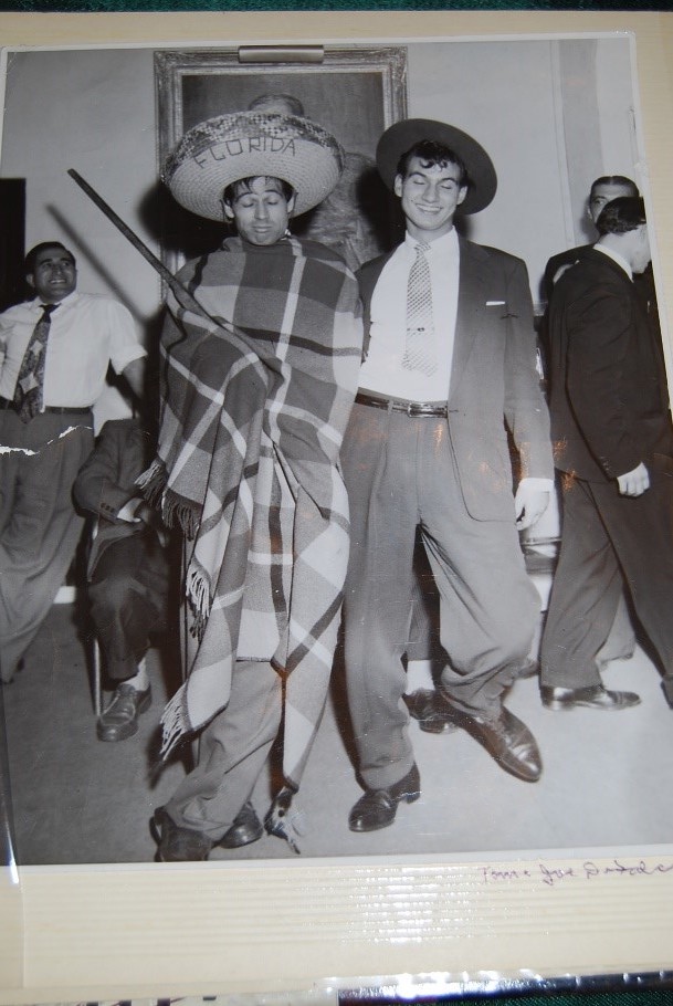 A black and white photo of two men, one wearing a suit and one wearing a hat inscribed with Florida and holding a gun.