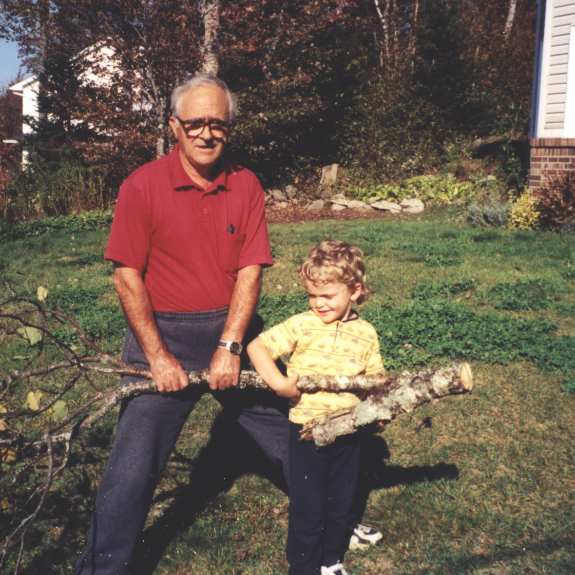 Young boy and man carrying tree branch.