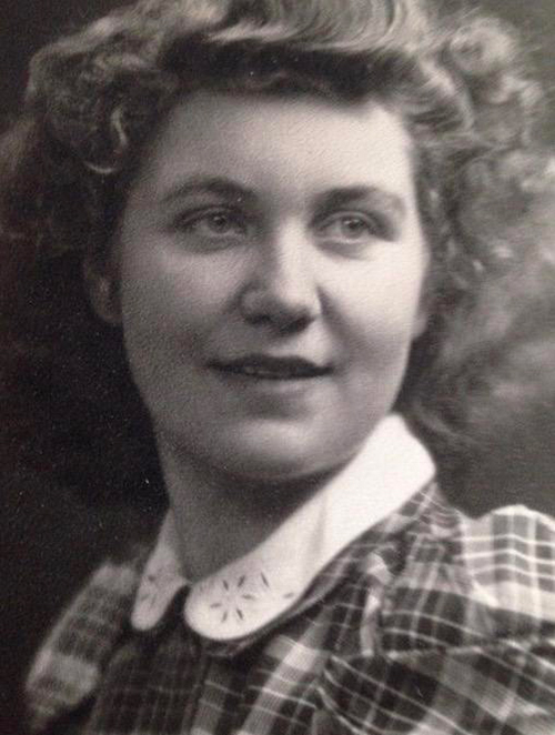 A young woman in a gingham dress smiles at the camera.