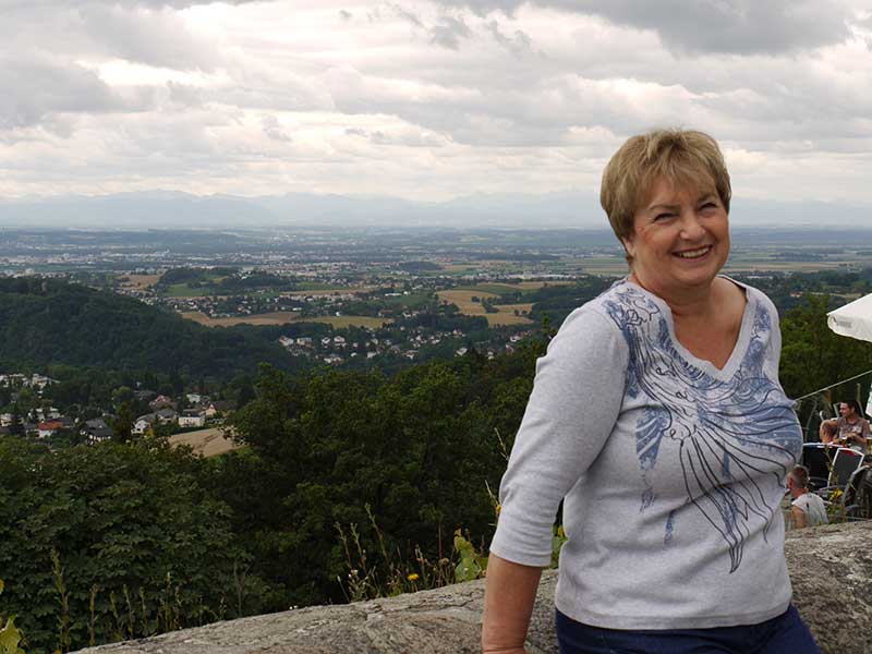 Recent photo of a woman leaning against a brick wall, and beautiful scenery behind her.