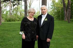 Recent photo of older Ivan and Helga, standing on green grass by trees.