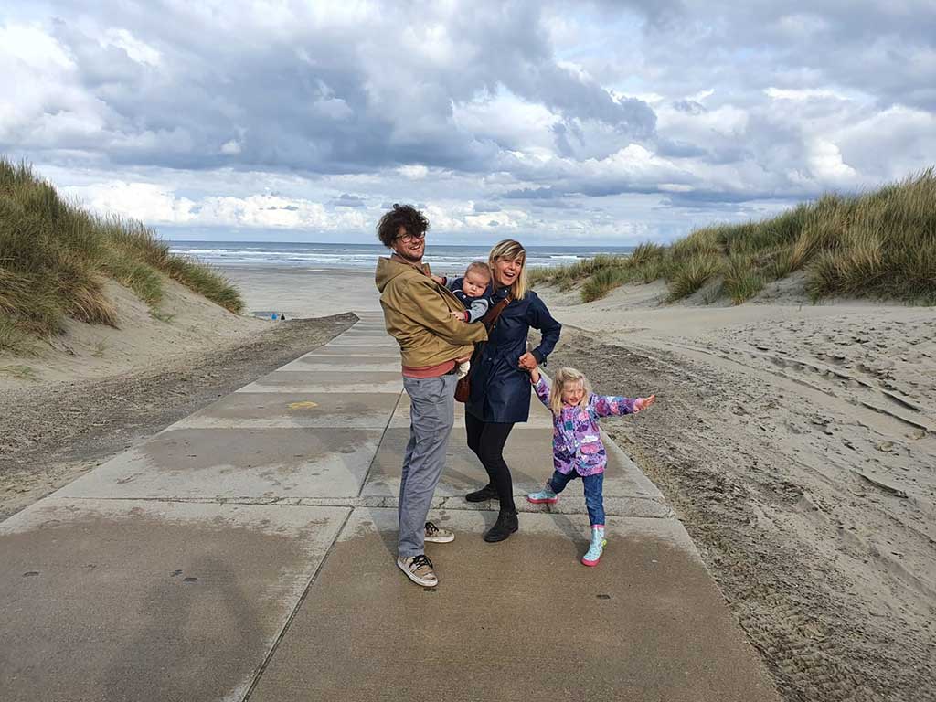A young couple with small children stand on a boardwalk at the beach.