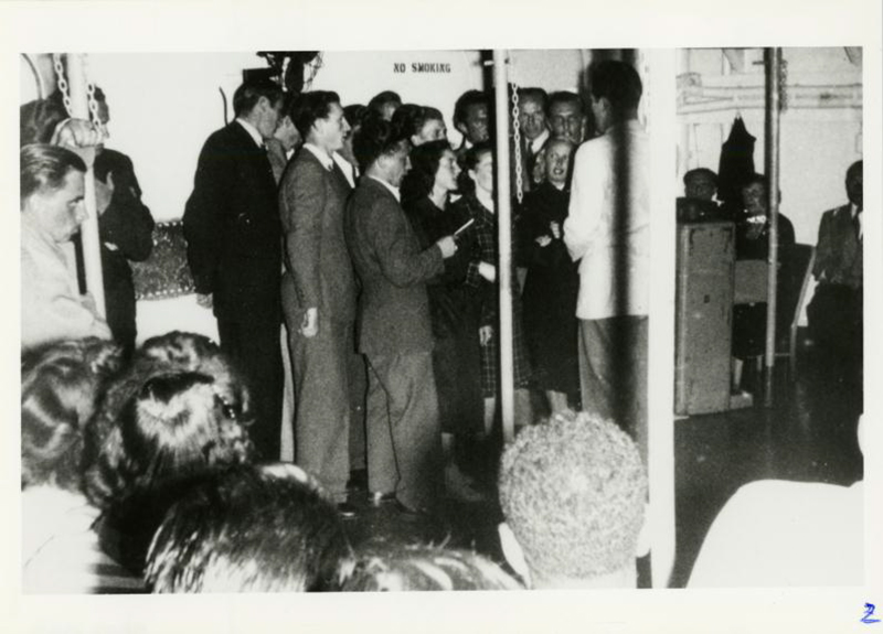 A man is talking to a group of people on the deck of a ship.
