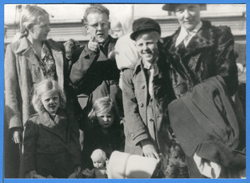 Old black and white photo of adults and children standing outside.