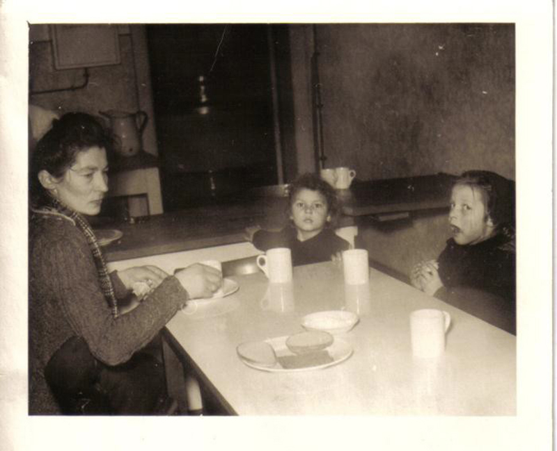 A young woman with two children sitting around the dinner table, which has three cups and bread on it.
