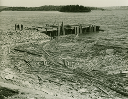 Aerial view of three men near a dock by the water, debris in the water.