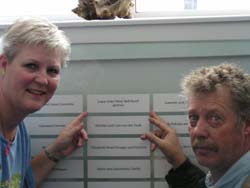 Man and woman pointing to a plaque on the Wall of Honour at Pier 21.