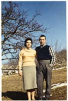 Man and woman standing on a dirt road in front of a tree. 