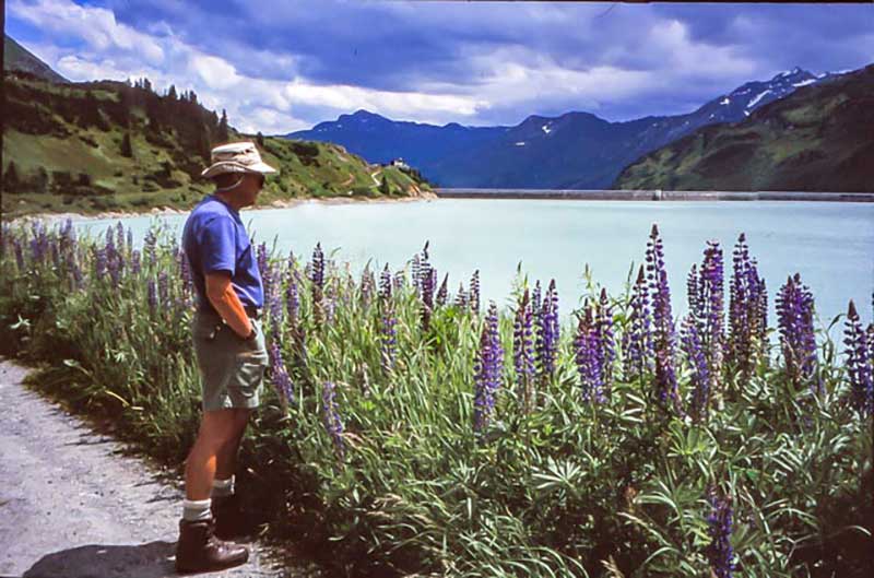 A man in summer clothing looks out over a beautiful lake.