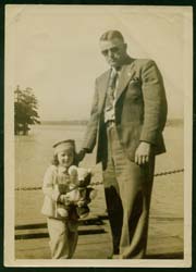 Gerald wearing sunglasses, standing with his young daughter who is holding a teddy bear.