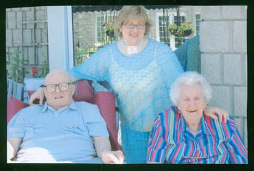 Recent color photograph of the elderly Wilson and their granddaughter, taken outside.