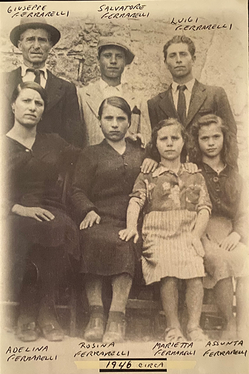 Very old photograph of women seated with men standing behind them, all of them unsmiling.