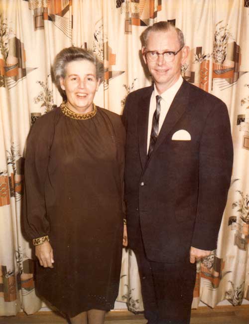 Well-dressed couple are standing in front of a backdrop.