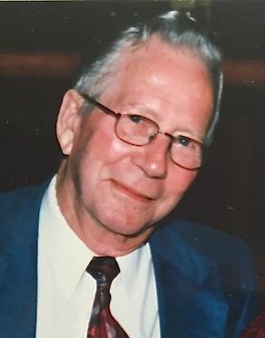 A portrait of a smiling older white man wearing glasses, a blue suit, and a red patterned tie.