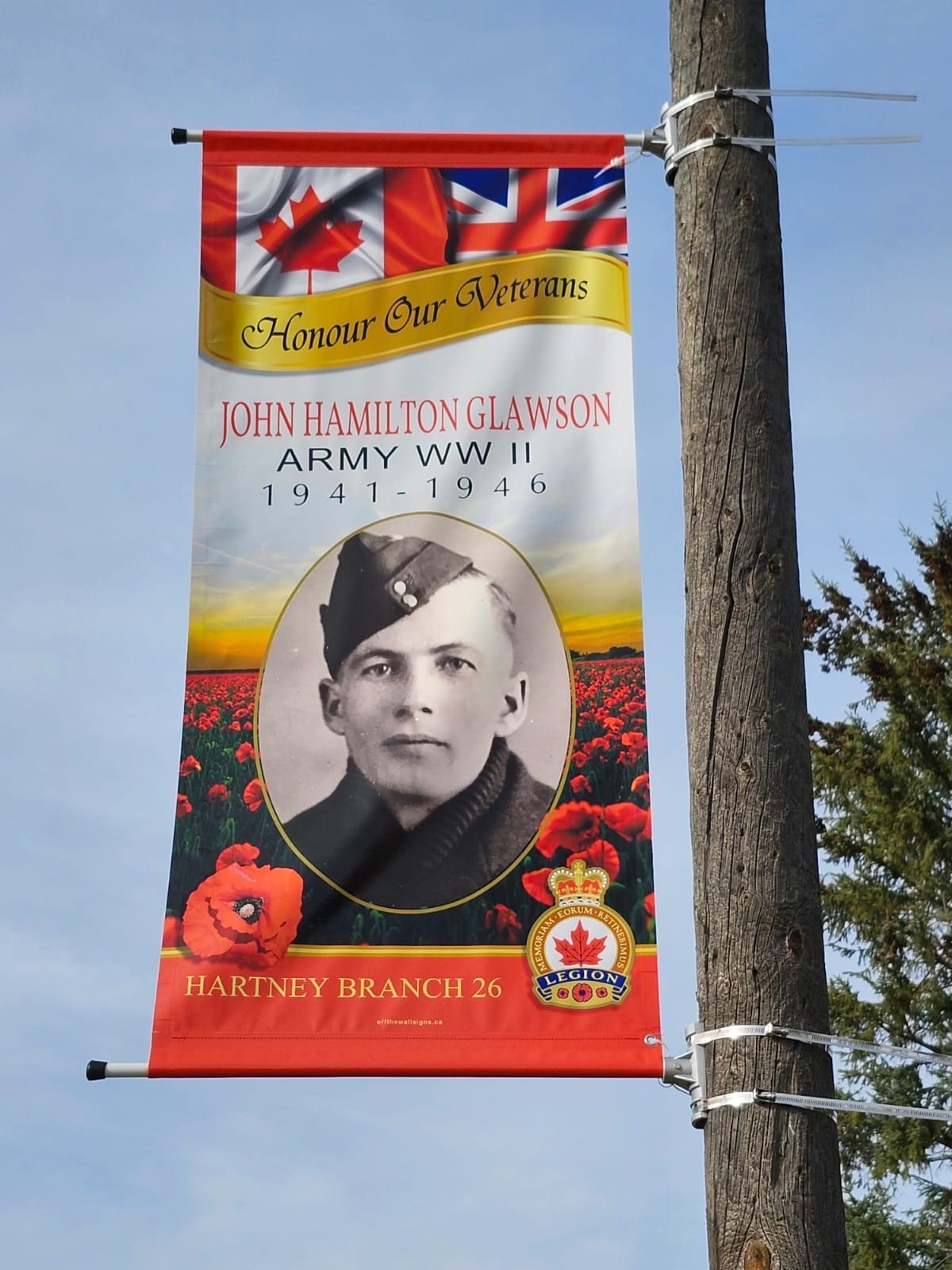 A colourful banner on a pole with a portrait of John Glawson and text stating Honour Our Veterans.
