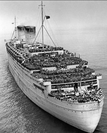 Black and white photo of a large ship in the water, with crowded masses of people on every deck.