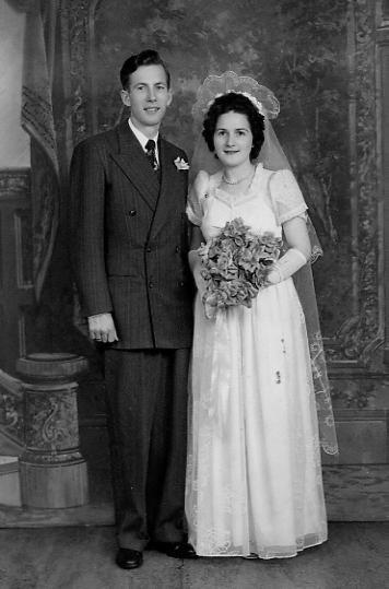 Black and white portrait of a smiling white couple on their wedding day, the bride holding a bouquet.