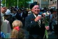 A smiling older white man in uniform carrying a bouquet of flowers, walking in a crowd of people.